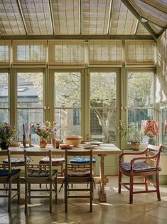 a dining room with large windows and wooden table surrounded by chairs, potted plants and vases