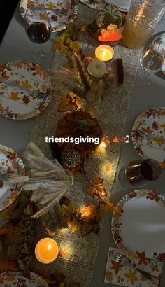 the table is set for thanksgiving dinner with candles and autumn leaves on it's placemats