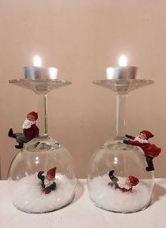 two clear glass vases with snow and santa figures in them on a white table