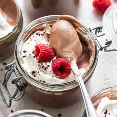 two jars filled with chocolate pudding and topped with raspberries, whipped cream and spoons