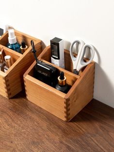 two wooden containers with scissors and other items in them sitting on a wood floor next to a white wall