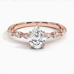 a rose gold engagement ring with a pear shaped center stone and side stones on the band