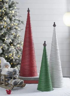 three small christmas trees sitting on top of a white table next to a christmas tree