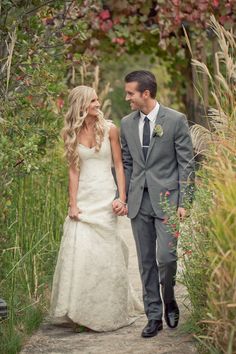 a bride and groom walking through the woods