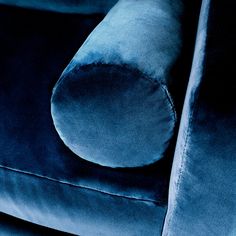 a blue velvet couch with an oval shaped pillow on it's backrest and arm rest