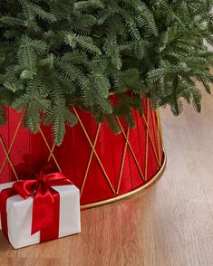 a christmas tree in a red pot with a white present box and ribbon tied around it