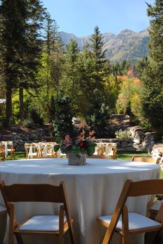 the table is set with white linens and wooden chairs for an outdoor function in the mountains