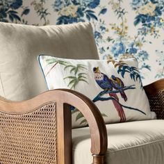 a chair with two pillows on top of it next to a flowered wallpaper