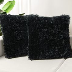 two black pillows sitting on top of a white couch next to a potted plant