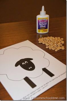 a paper cut out of a sheep with peanuts on the table next to it and a bottle of school glue