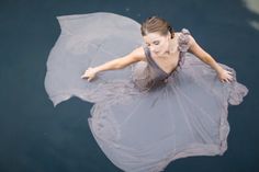 a woman floating on top of a body of water wearing a dress and holding an umbrella