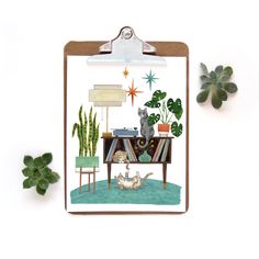 a clipboard with an image of a desk and cat on it next to plants