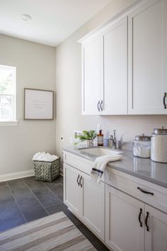 a kitchen with white cabinets and gray tile flooring, along with an area rug on the floor