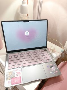 an open laptop computer sitting on top of a white table next to a pink pillow