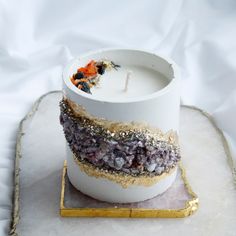 a white candle with gold and purple decorations on it, sitting on a marble tray