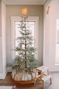 a small christmas tree sitting in front of a window next to a wooden chair and ladder