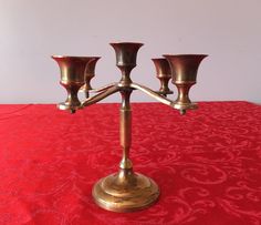 a brass candelabra on a red tablecloth with four candles in it