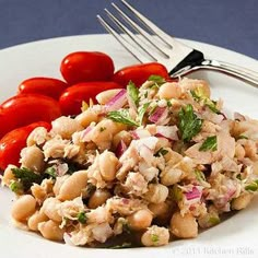 a white plate topped with pasta and tomatoes next to a fork on top of a table