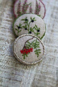 three embroidered buttons with red berries on them sitting on a piece of fabric, one is green and the other is pink