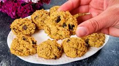 a person is picking up some oatmeal cookies on a white plate with purple flowers in the background