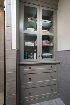 a cabinet with glass doors and drawers in a bathroom that also has towels on the shelves