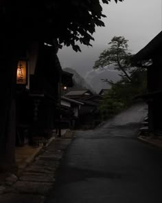 an empty street with buildings and trees on both sides in the dark, foggy weather