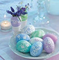 a plate topped with colorful eggs next to a vase filled with purple and blue flowers