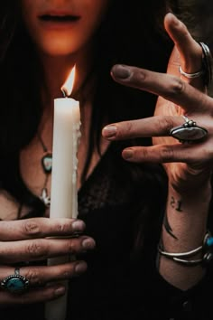 a woman holding a white candle with her hands in front of her face and wearing rings