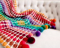 a multicolored crocheted blanket with pom - poms sits on a white couch