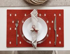 a place setting with silverware and napkins on a red place mat next to a white plate