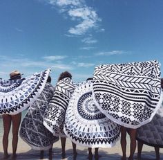 four people standing in front of an array of umbrellas on the beach, with their backs turned to the camera