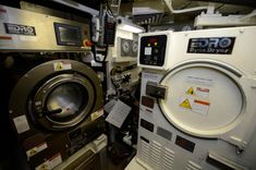 an industrial washing machine with its door open and labels on the front, next to other machines