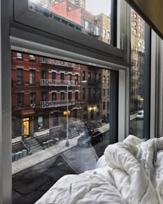 an unmade bed sitting in front of a window next to a tall building with lots of windows