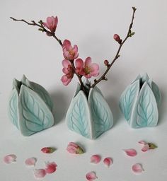 three small vases with flowers in them on a white surface, next to petals