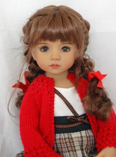 a doll wearing a red cardigan and plaid skirt with her hair in pigtails