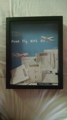 there is a framed poster on the bed with some papers in front of it that says, come fly with me