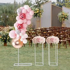 some pink and white balloons are on poles in the grass next to chairs with flowers