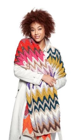 a woman wearing a multicolored knitted shawl and white coat with her arms crossed