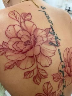 the back of a woman's shoulder with flowers and words on her left side