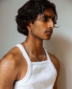 a young man wearing a white tank top and silver necklace with an earring on his neck