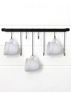 three coffee cups hanging from hooks on a white wall with black metal bar and pegs