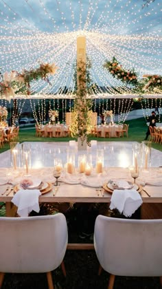 a table set up for a wedding with candles on it and lights strung from the ceiling