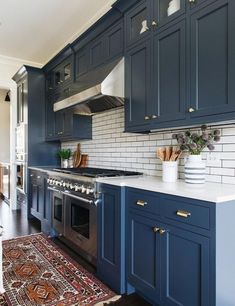 a kitchen with dark blue cabinets and white subway backsplash, gold pulls on the hood