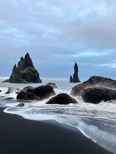 some very pretty rocks in the water by the beach with waves crashing on them and one rock sticking out of the water