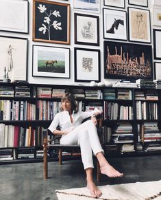 a woman sitting on a chair in front of a bookshelf filled with pictures