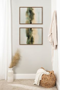 two paintings hang on the wall above a basket in a room with white walls and carpet