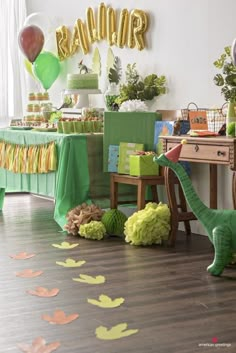 a dinosaur birthday party with balloons, streamers and paper leaves on the floor in front of it