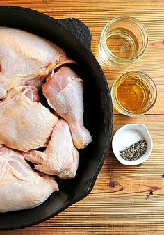 raw chicken in a skillet with spices and seasoning next to it on a wooden table