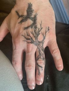 a person's hand with a tree tattoo on it and two birds flying around