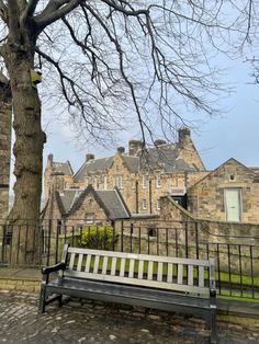 a wooden bench sitting next to a tree in front of a stone building with many windows